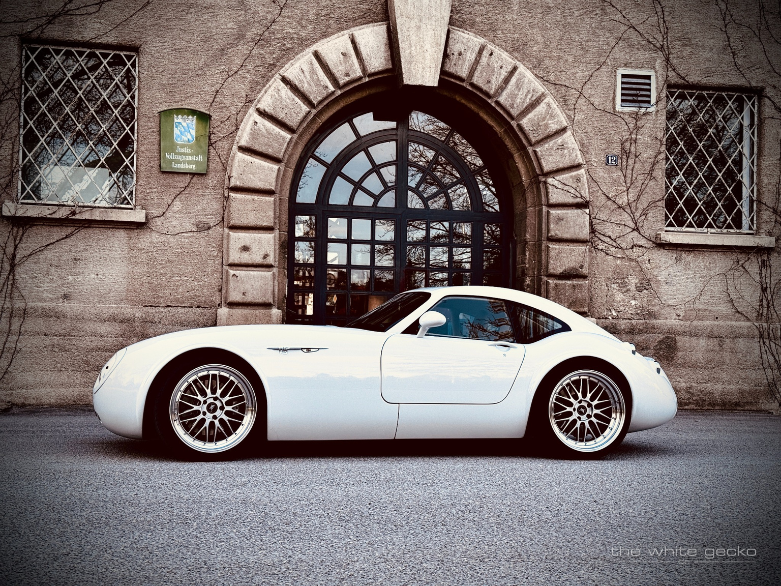 Seitliches Profil des weißen Wiesmann MF4 GT No.180 vor dem markanten Tor des Gefängnisses in Landsberg